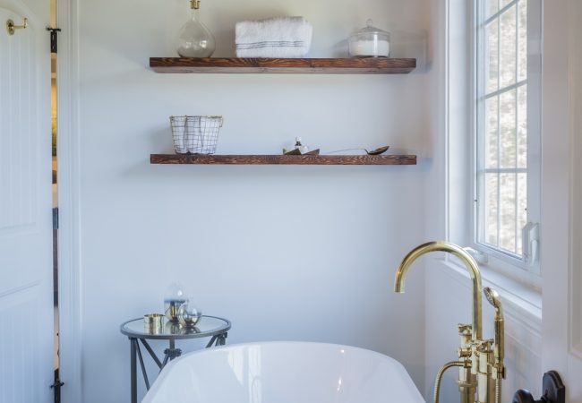Updated bathroom with freestanding tub, gold finishes, and built-in shelves (JM Construction)