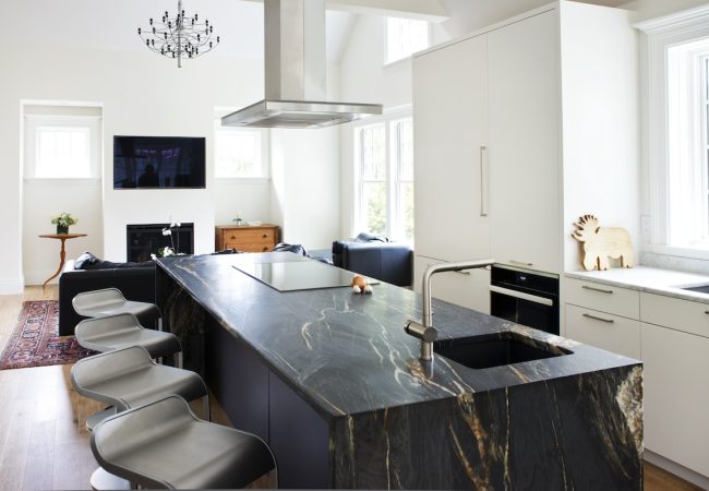Custom kitchen with granite island, cooktop, ceiling hood, custom cabinets, and open seating (JM Construction)
