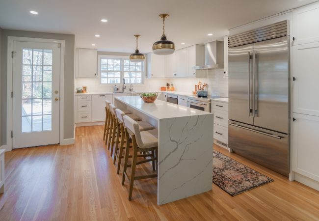 Updated kitchen with large sit-down island, double-door fridge, wood floors, and steps to backyard (JM Construction)