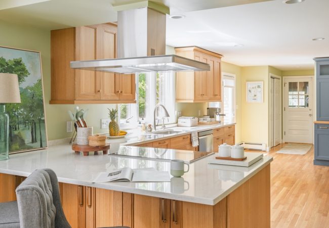 Open floor plan kitchen with large island, wood cabinets, and cooktop with overhead range hood (JM Construction)