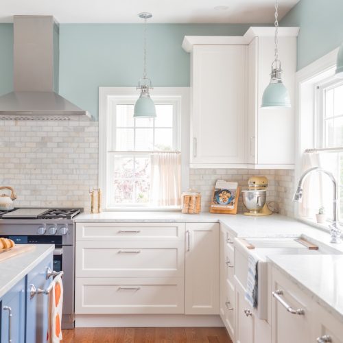 Updated kitchen with island, bright windows, ceiling hood, white granite countertops, and white cabinets (JM Construction)
